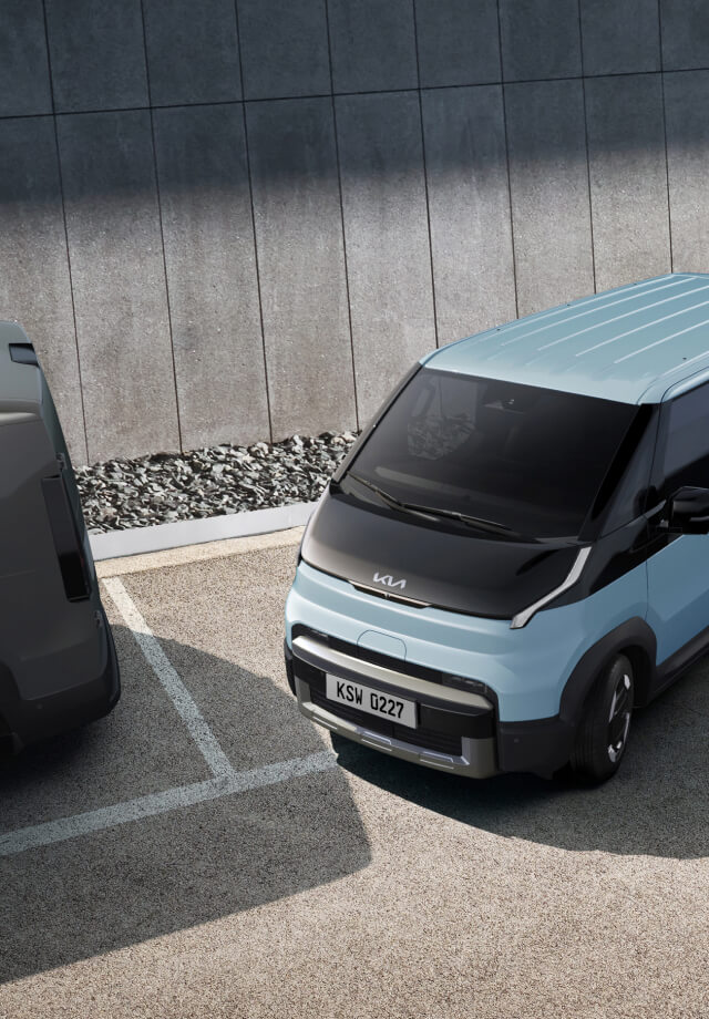 Der Kia PV5 Passenger fährt aus einer Parallelparklücke – auf einem Parkplatz mit zwei weiteren Kleinbussen.